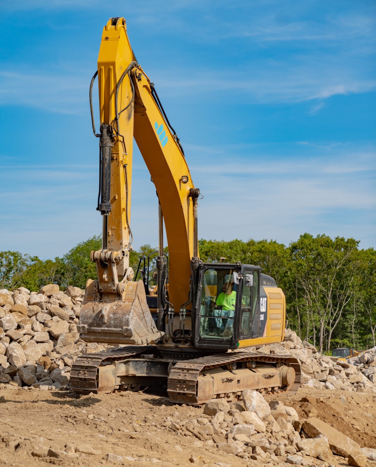 Excavator and operator beside a rock pile at the Applied Materials Logistics expansion site.