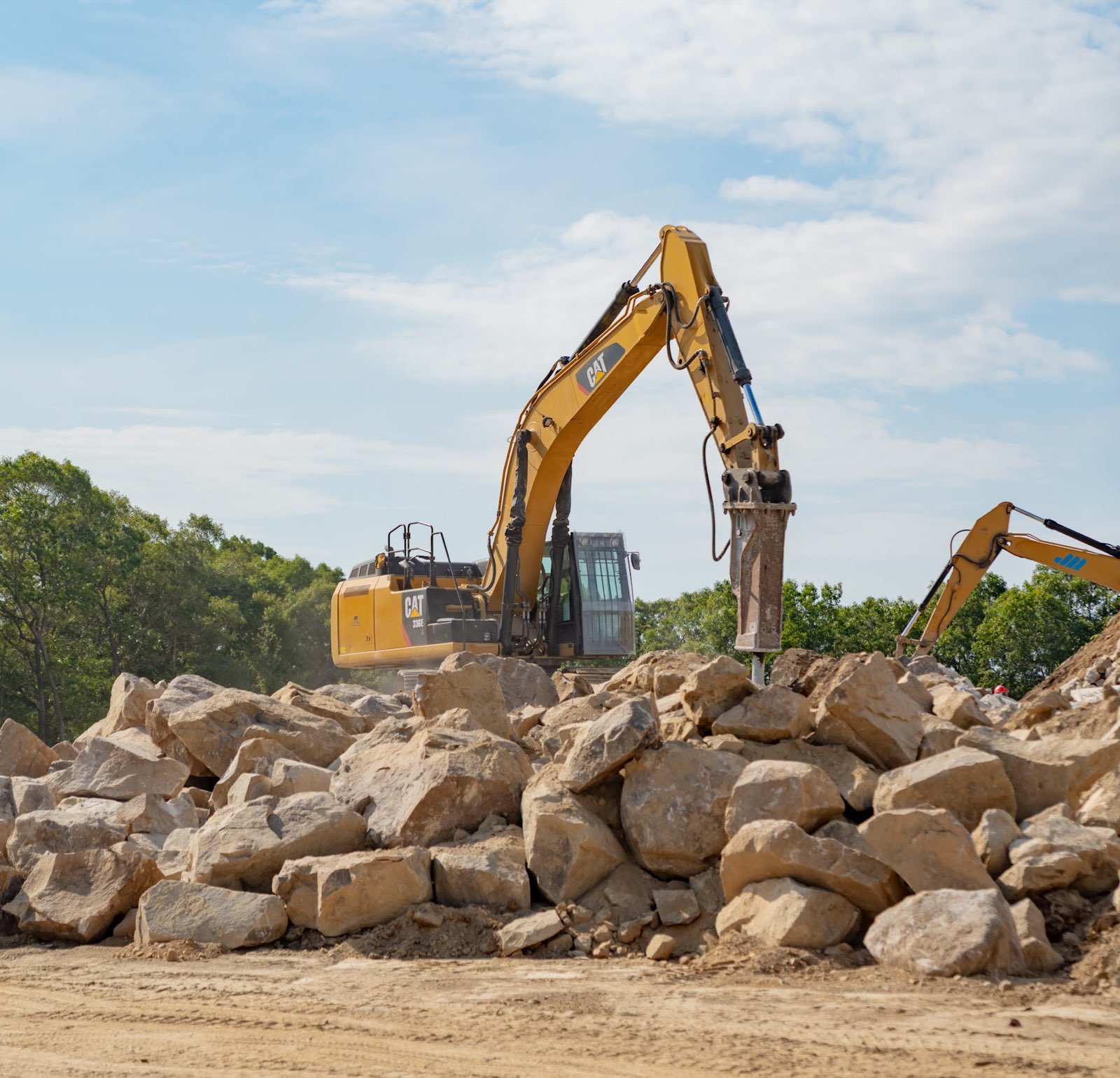 Excavator with a hydraulic breaker working among large rocks at the Applied Materials site.