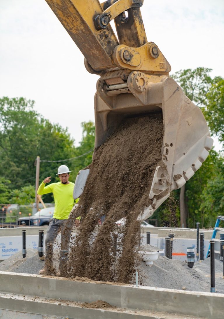 Excavator bucket placing fill inside the Raising Cane’s foundation around underslab utility piping.