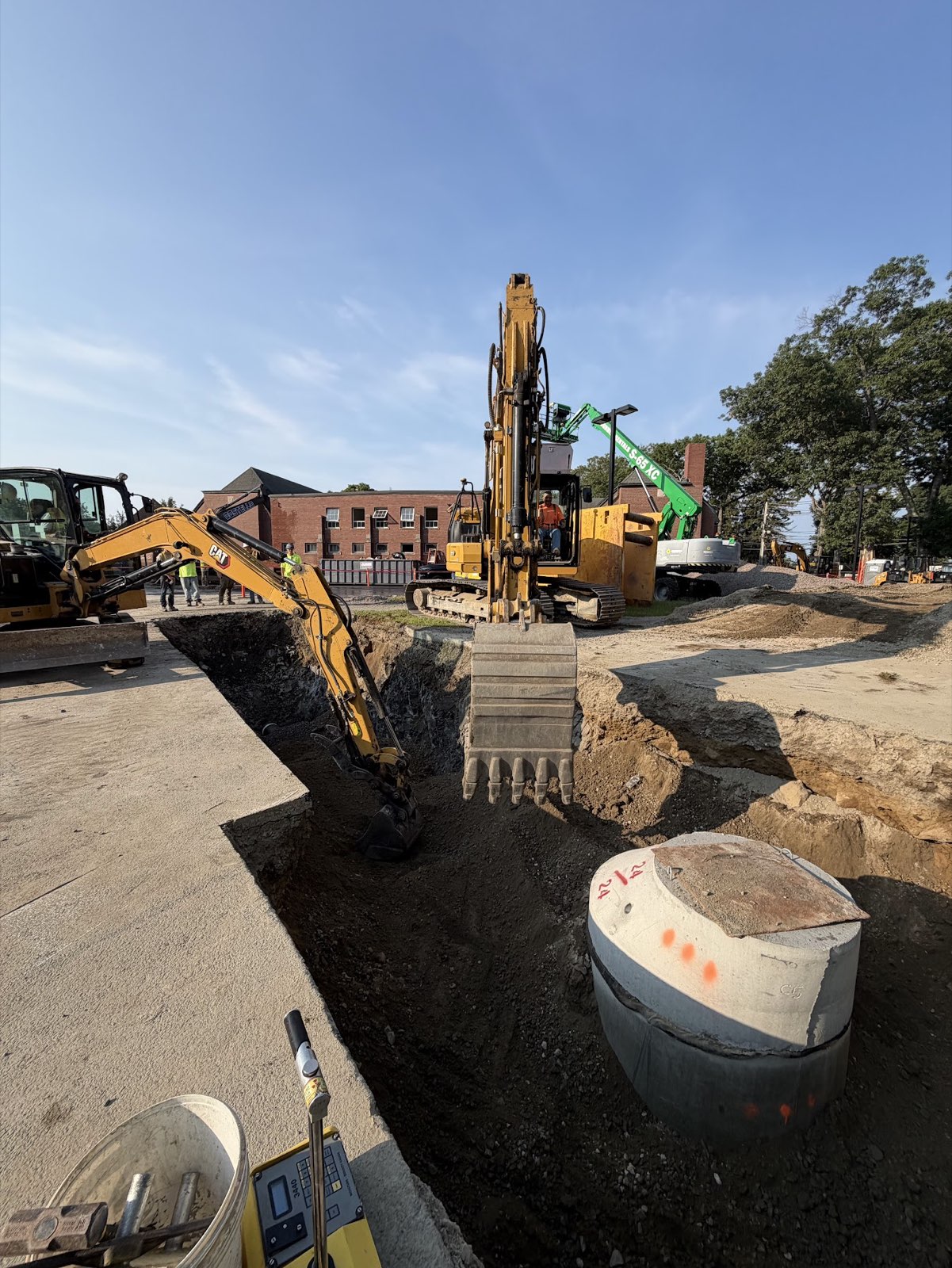 Excavators working in a utility trench beside a concrete structure at St. John’s Prep Memorial Hall.