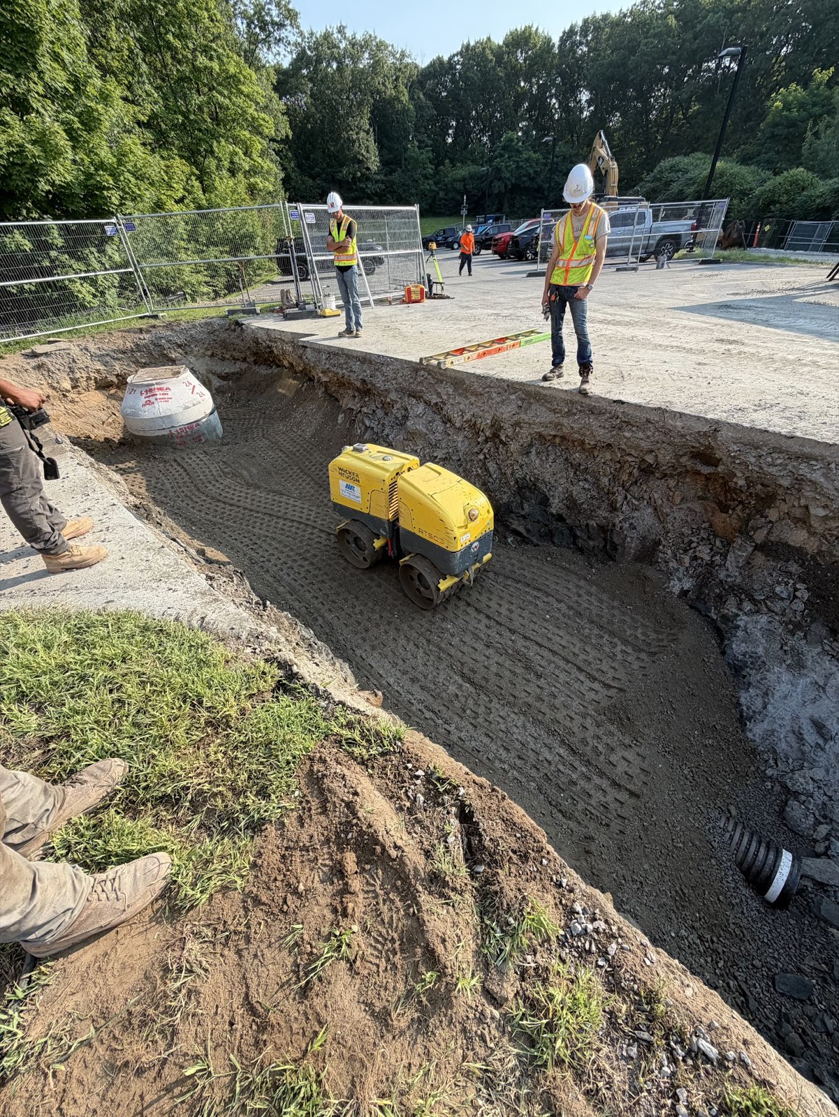 Construction crew monitoring a trench compactor near drainage piping at St. John’s Prep Memorial Hall.